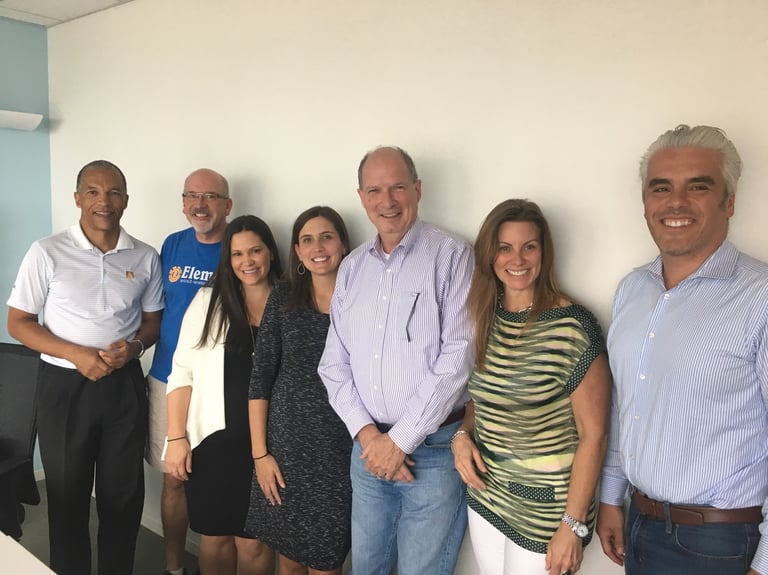Group of seven smiling professionals posing together in front of a white wall