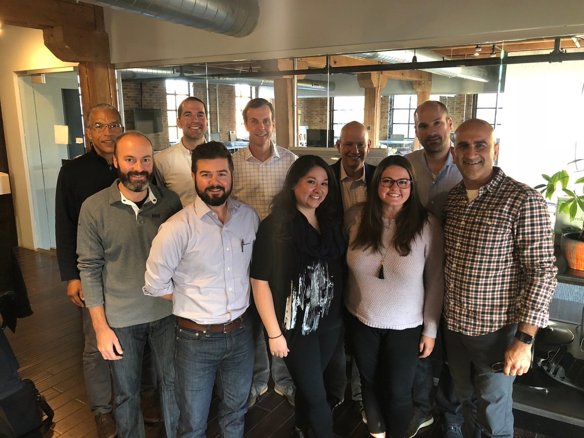 Group of 12 colleagues standing together in an office, smiling at the camera in a casual team photo